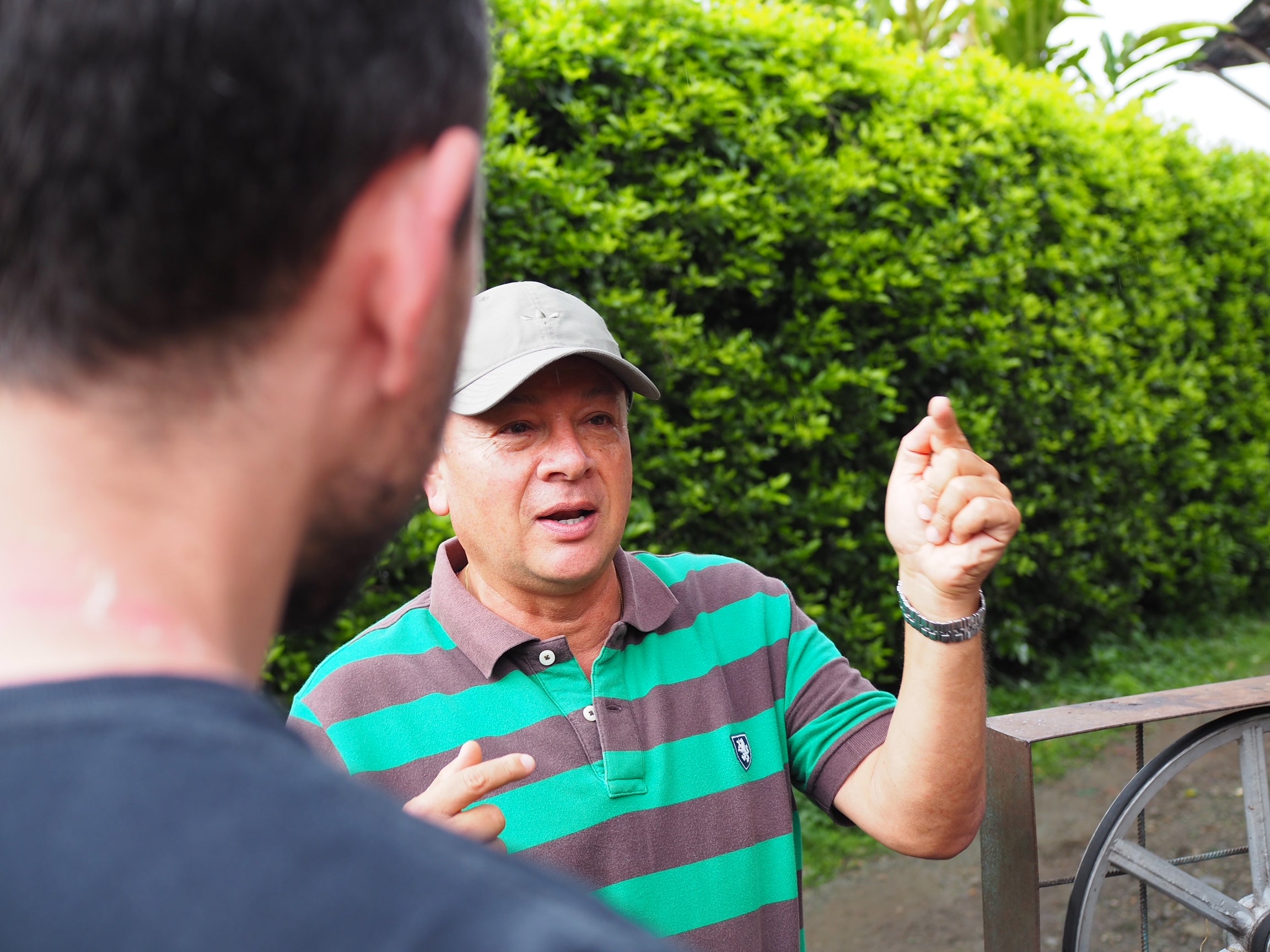 Con camiseta a rayas verdes y marrones, y ataviado de una gorra vemos a Jairo, ingeniero agrónomo y uno de los dueños de la finca cafetera Puerto Alegre, en Colombia, dar explicaciones sobre algo. 